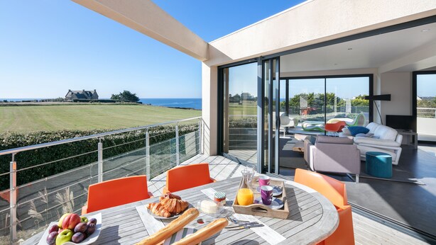 Un balcon avec une table préparée pour le petit-déjeuner, donnant sur une pelouse et un plan d’eau.