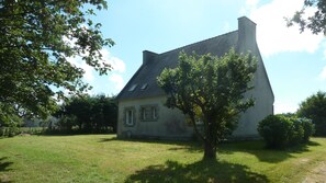 Ein zweistöckiges Haus mit geneigtem Dach, Schornstein und einem kleinen Vorgarten mit einem Baum.