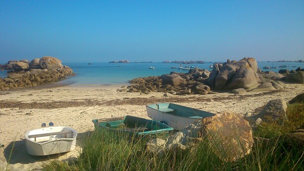 Platja amb vaixells, roques grans i aigua blau cel.
