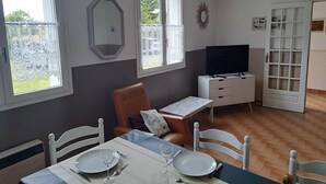 Zona de menjador amb una taula preparada per a dues persones, una televisió i una porta que dona a una altra habitació.