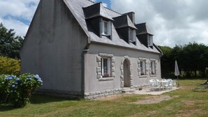 Una casa amb un teulat a dos vessants pronunciat, emmarcadors de finestra de pedra i un petit porxo amb seients exteriors.