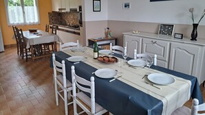 Zona de menjador amb taula preparada per a quatre, caires blancs, cuina al fons i un quadre encimbellat a la paret.