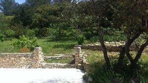 Un muro in pietra con un pilastro, circondato da vegetazione e un cielo sereno.