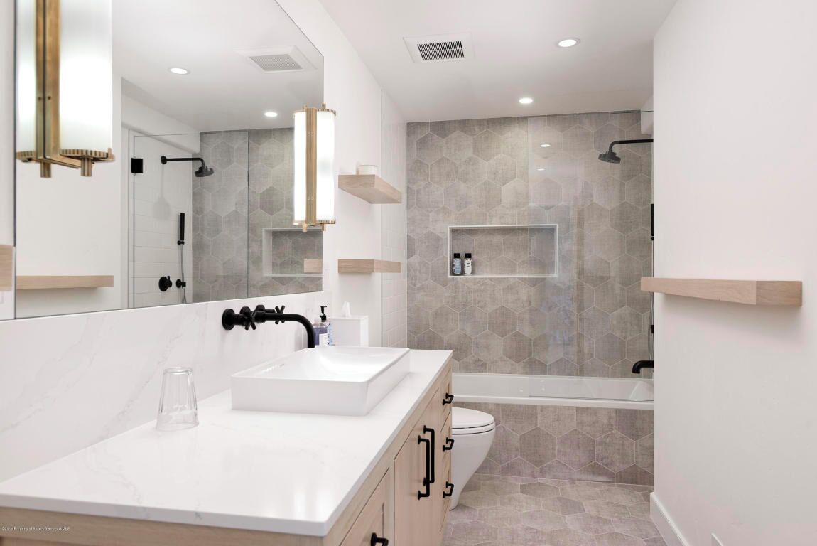 A modern bathroom with a large mirror, a white sink, a bathtub, and a shower area.