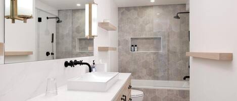 A modern bathroom with a large mirror, a white sink, a bathtub, and a shower area.