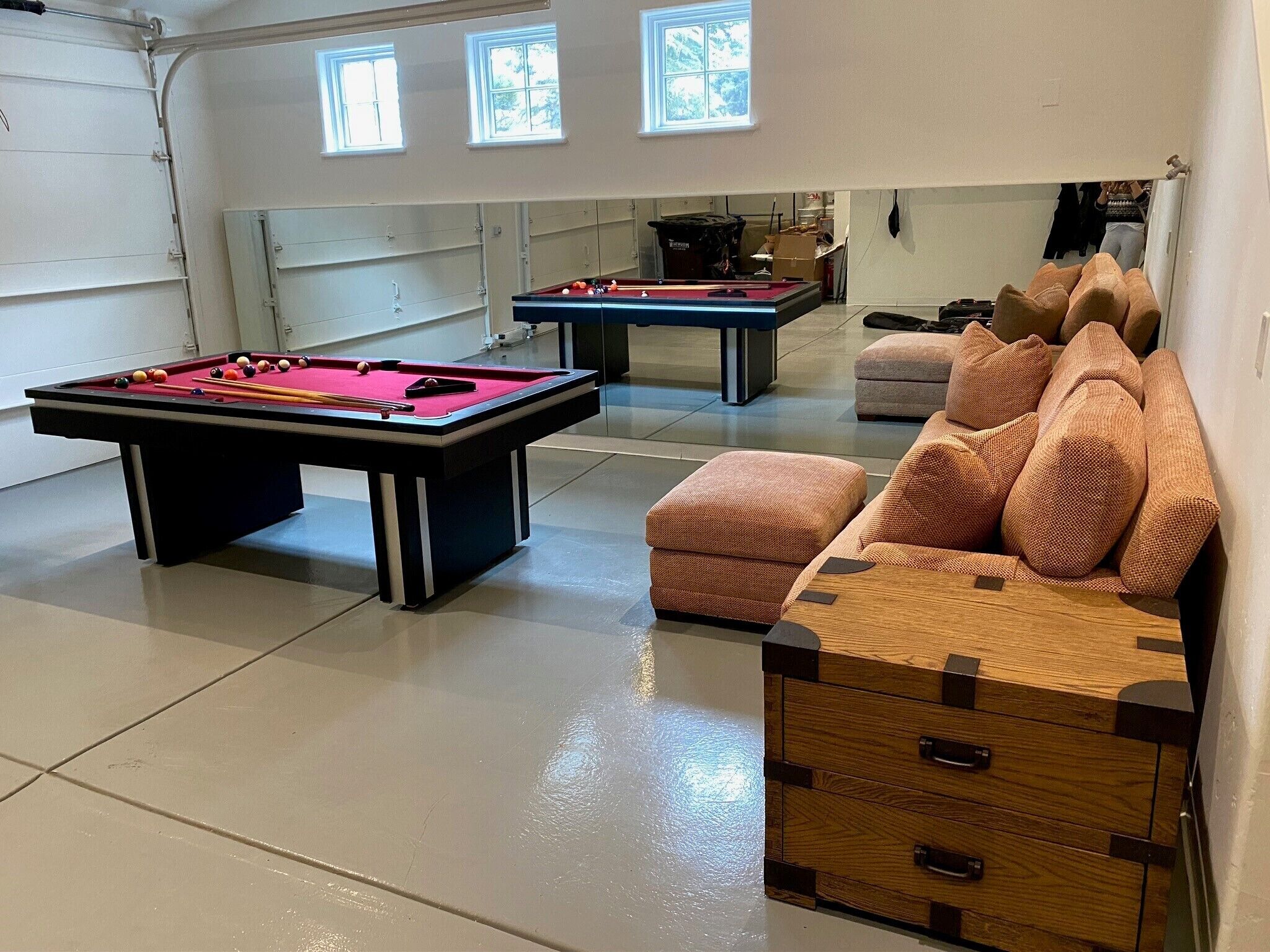 A pool room with two pool tables, a cushioned seating area, and a garage door.