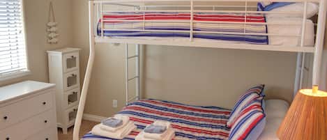 Una cama individual superpuesta con una colcha a rayas, una lámpara de noche y un pequeño aparador.