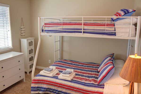 A bunk bed with a striped bedspread, a bedside lamp, and a small dresser. - Carlsbad Beach Cottage - Near Beach, Village and Legoland (Carlsbad)