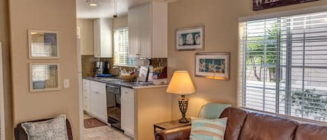 A compact living space with a kitchenette, a brown leather couch, a lamp, and a 'WELCOME' sign.