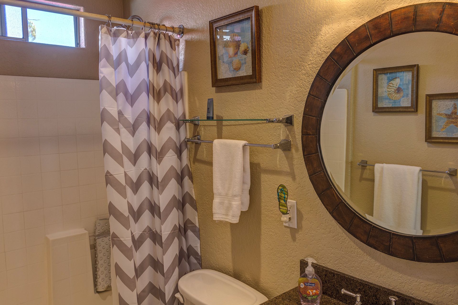 Une salle de bain avec un rideau de douche, des toilettes, un lavabo avec un distributeur de savon, un porte-serviettes et un miroir avec un cadre décoratif.