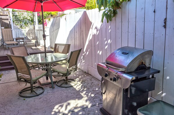 An outdoor patio with a round glass table, four wicker chairs, and a stainless steel grill.