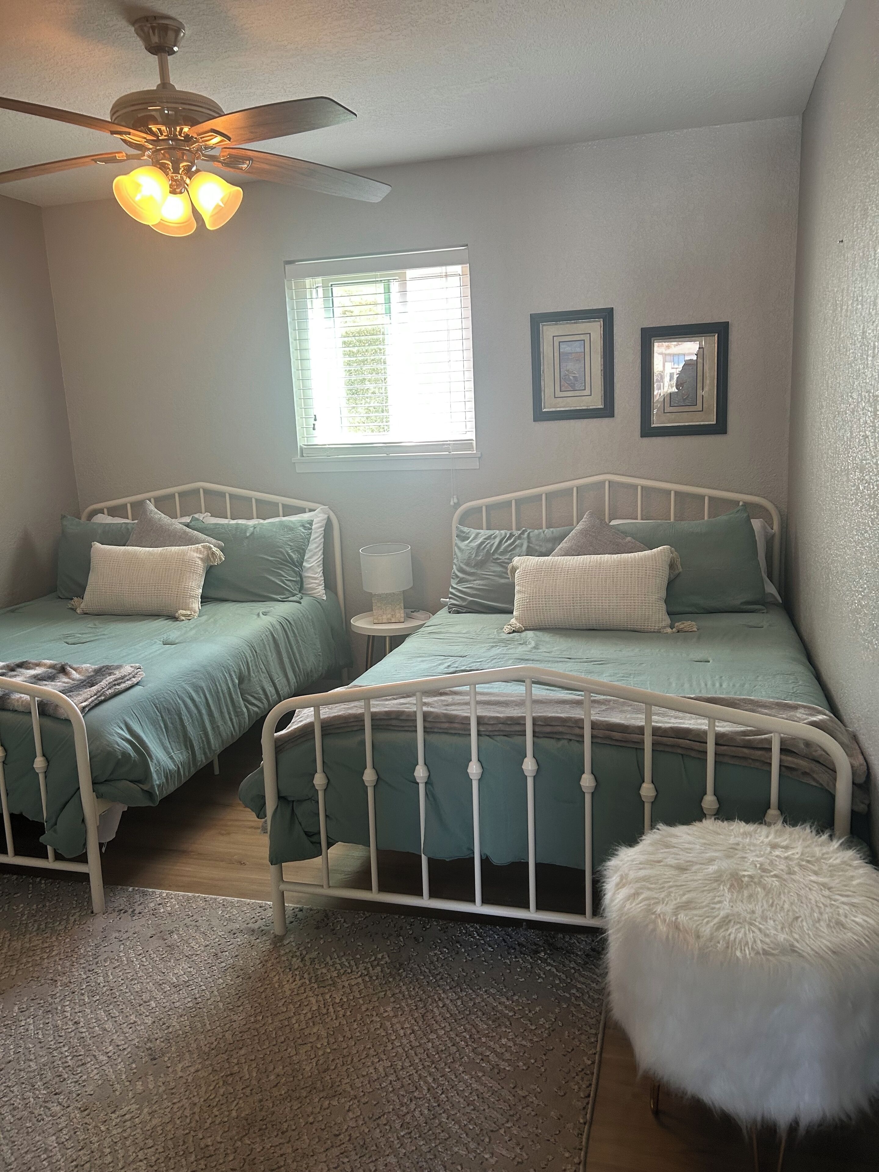 A bedroom with two twin beds, a ceiling fan, a window, and a small table.