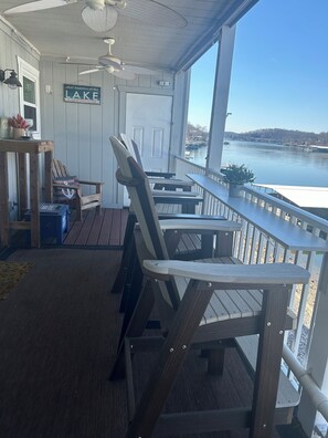 Una terraza techada con sillas y mesas de madera, un cartel que dice 'what happens at the lake is laughed about all year', y vista a un lago.