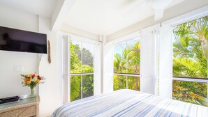 Un dormitorio con una cama grande, un televisor de pantalla plana, un aparador y una ventana con vista a la vegetación tropical.