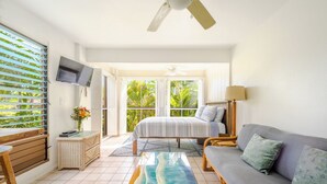 Una habitación luminosa con cama, sofá, televisión y ventana con persianas.