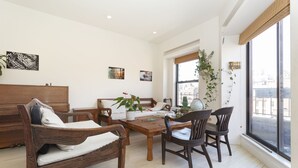 A living room with a wooden sofa, a wooden table, and a wooden chair. There are plants on the table and a window with a view of buildings. - Beautiful apartment with balconies and views, near park and museums in Nolita (New York)
