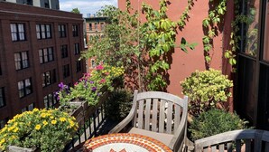 A small outdoor seating area with a mosaic-tiled table and chairs, surrounded by potted plants and flowers. - Beautiful apartment with balconies and views, near park and museums in Nolita (New York)