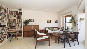A spacious room with a large bookshelf, a wooden piano, a dining table with chairs, and a large window. - Beautiful apartment with balconies and views, near park and museums in Nolita (New York)