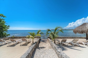 A beachside view with lounge chairs and a thatched umbrella, leading to the sea.