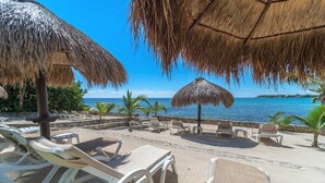 Un espace de détente aménagé sur la plage, avec des parasols en chaume, des chaises longues et une vue sur l’océan.