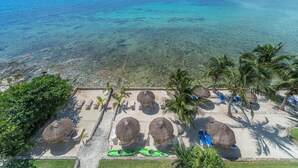 Un complexe hôtelier de bord de mer doté de parasols en chaume, de chaises longues et offrant une vue dégagée sur l’océan.
