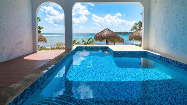 Une piscine avec vue sur l’océan et des parasols en chaume.
