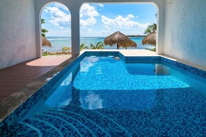 A swimming pool with a view of the ocean and thatched umbrellas.