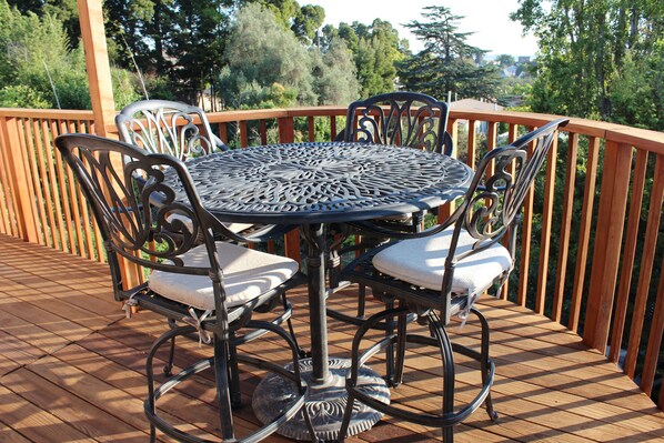 A round outdoor table with chairs on a wooden deck, surrounded by a wooden railing.