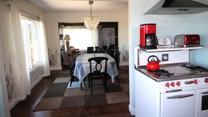 Une cuisine équipée d’une cuisinière, d’une machine à café et d’un grille-pain. On y trouve une table à manger avec des chaises et un lustre.