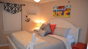 Ein Schlafzimmer mit Bett, Nachttisch, Lampe, einem Gemälde und einem Schild mit der Aufschrift 'BEACH HOUSE'.