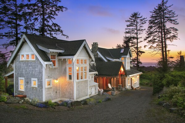 A large, two-story house with a stone facade and multiple windows, surrounded by trees and a gravel driveway. - OCEANFRONT PROPERTY - Black Rock Beach House (Ucluelet)