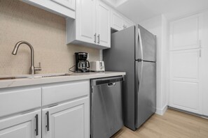 A kitchen with white cabinets, a stainless steel refrigerator, a coffee maker, and a dishwasher.