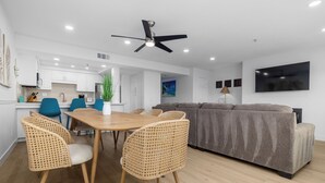 Un salon moderne avec un canapé gris, une table à manger entourée de chaises en osier et un ventilateur de plafond.