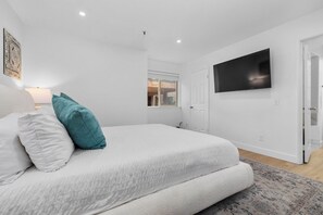 A bedroom with a bed, a television mounted on the wall, and a window.
