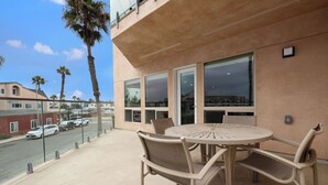 Un balcon avec une table ronde et des chaises, donnant sur une rue bordée de voitures garées et de palmiers.