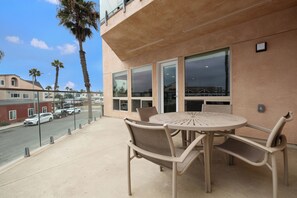 A balcony with a round table and chairs, overlooking a street with parked cars and palm trees.