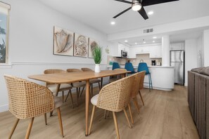 A modern kitchen with white cabinets, a central island, and a dining area with a wooden table and wicker chairs.