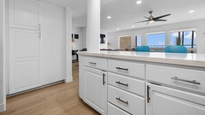Une cuisine moderne avec des meubles blancs, un plan de travail en marbre et un ventilateur de plafond.