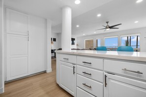 A modern kitchen with white cabinetry, a marble countertop, and a ceiling fan.