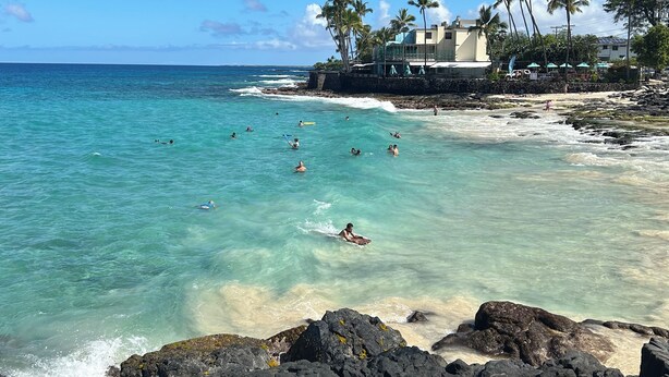 A coastal scene with clear turquoise water, rocky shoreline, and a building with a balcony overlooking the beach. - 
Kona coast studio, great rates free HS-WIFI, Parking, Walk to Magics Beach (Kailua-Kona)