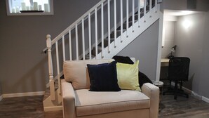 A beige sofa with three pillows in a room with a wooden floor and a white staircase. - Luxury Apartment Close to Mayo and St. Mary s......... (Rochester)