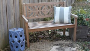 A wooden bench with a cushion, a blue stool with holes, and a wooden fence in the background. - Luxury Apartment Close to Mayo and St. Mary s......... (Rochester)