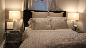 A neatly made bed with two bedside lamps, a framed picture, and a clock on the nightstand. - Luxury Apartment Close to Mayo and St. Mary s......... (Rochester)