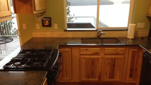 Cocina con armarios de madera, un lavamanos de acero inoxidable y una estufa a gas.