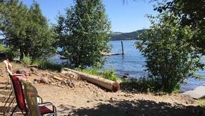 Un camping junto a un lago, con sillas y un tronco de madera.