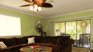 A living room with a brown leather sofa, a glass coffee table with magazines, and a ceiling fan. - Only 3-Miles to Gulf Beaches - Swim, Play Tennis or Just Relax (Bonita Springs)