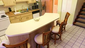 A kitchen with wooden cabinets, a microwave, a refrigerator, a sink, and a white countertop. There are four wooden chairs with cushioned seats. - Only 3-Miles to Gulf Beaches - Swim, Play Tennis or Just Relax (Bonita Springs)