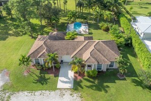 A single-story house with a tiled roof, surrounded by a well-maintained lawn and palm trees.