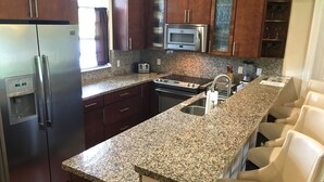 A modern kitchen with granite countertops, stainless steel appliances, and dark wooden cabinets. - Swans Nest West - Modern & Private, Heated Pool, 3 Brm (Lake worth)