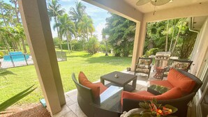 A covered patio area with wicker furniture, a small table, and a potted plant. - Swans Nest West - Modern & Private, Heated Pool, 3 Brm (Lake worth)